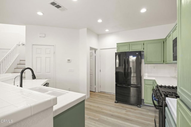 kitchen featuring tile countertops, backsplash, black appliances, and green cabinetry