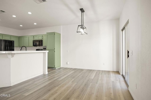 kitchen featuring decorative light fixtures, light hardwood / wood-style floors, black appliances, green cabinets, and a breakfast bar area