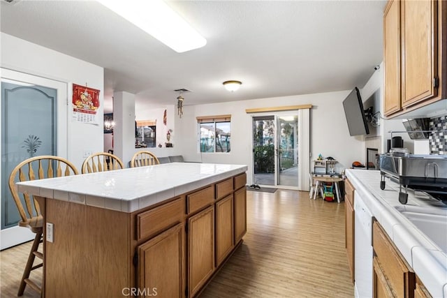 kitchen with a breakfast bar, white dishwasher, light hardwood / wood-style floors, and a center island