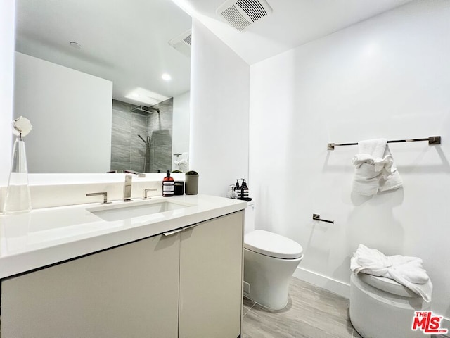 bathroom featuring toilet, vanity, a tile shower, and hardwood / wood-style flooring