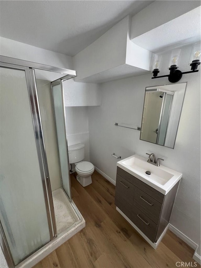 bathroom with wood-type flooring, walk in shower, vanity, and toilet