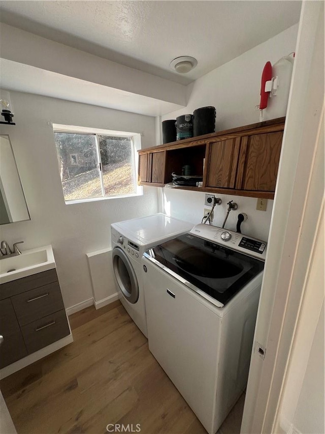 washroom featuring cabinets, sink, washer and clothes dryer, and light wood-type flooring