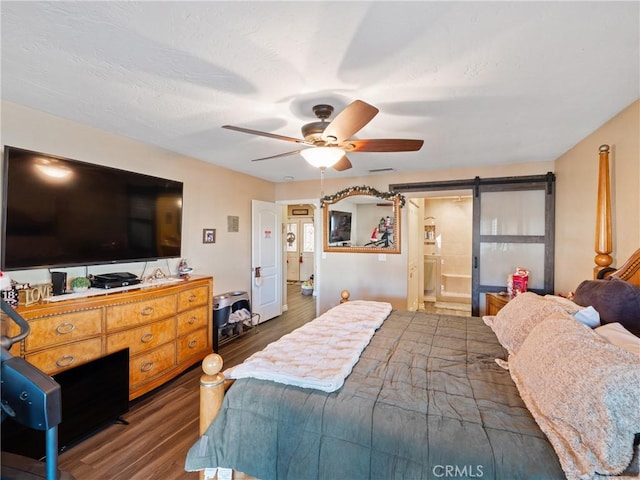 bedroom featuring connected bathroom, ceiling fan, a barn door, and dark hardwood / wood-style floors