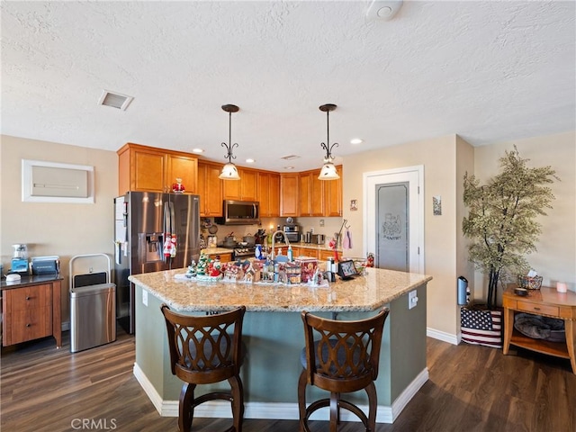 kitchen featuring light stone counters, appliances with stainless steel finishes, dark hardwood / wood-style flooring, and hanging light fixtures