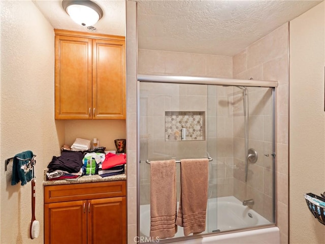 bathroom with a textured ceiling and bath / shower combo with glass door