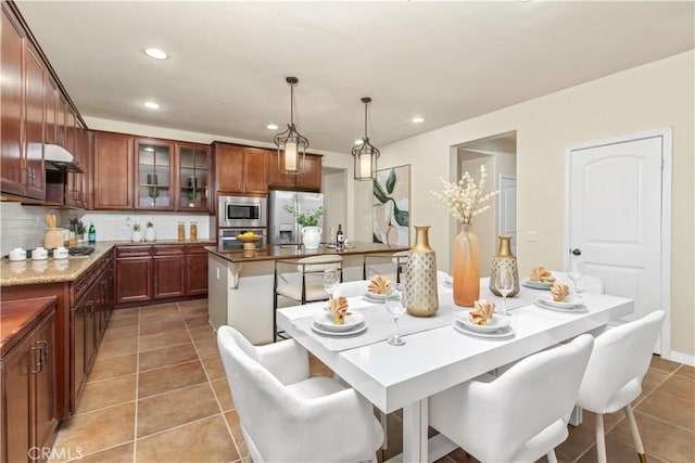 kitchen with decorative light fixtures, tasteful backsplash, tile patterned floors, appliances with stainless steel finishes, and a breakfast bar area