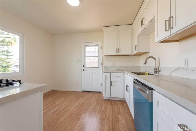 kitchen with light stone countertops, white cabinets, light hardwood / wood-style floors, sink, and stainless steel dishwasher