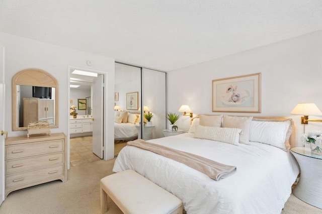 bedroom featuring light colored carpet, a closet, and ensuite bath