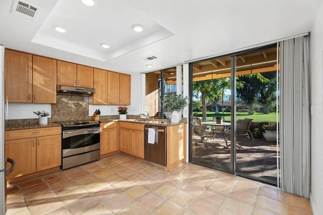 kitchen with decorative backsplash, appliances with stainless steel finishes, dark stone countertops, and a tray ceiling