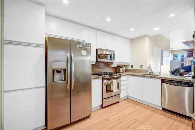 kitchen featuring stainless steel appliances, white cabinets, light stone counters, and sink