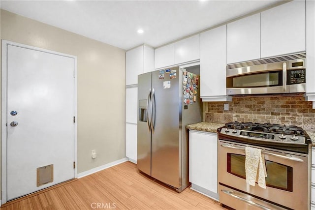 kitchen featuring tasteful backsplash, white cabinetry, light wood-type flooring, appliances with stainless steel finishes, and light stone counters