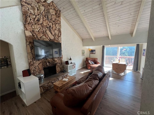 living room with vaulted ceiling with beams, wood-type flooring, a stone fireplace, and wooden ceiling