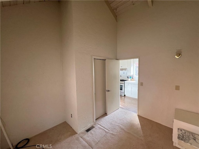 hallway with light carpet, beam ceiling, and high vaulted ceiling