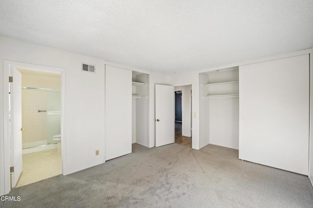 unfurnished bedroom featuring ensuite bathroom, carpet floors, a textured ceiling, and two closets