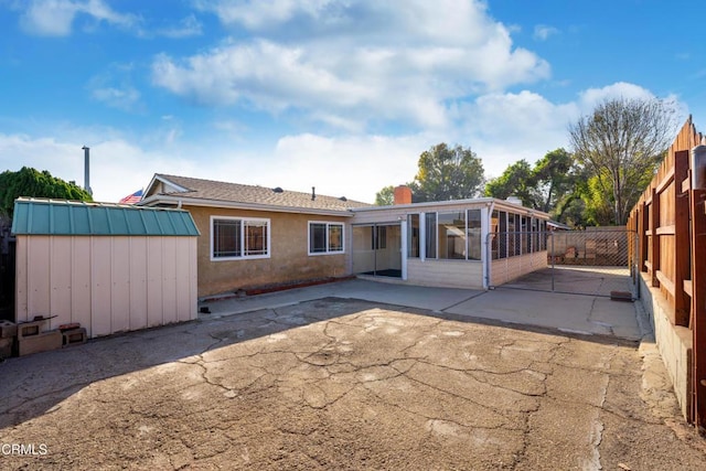 rear view of property featuring a sunroom, a storage shed, and a patio