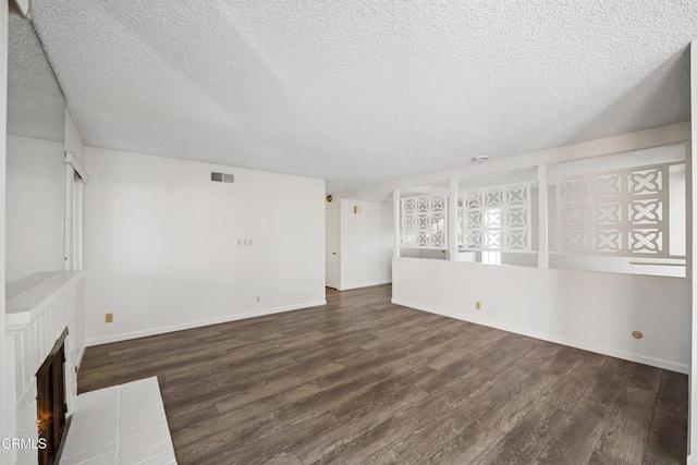 unfurnished living room featuring a brick fireplace, dark wood-type flooring, and a textured ceiling