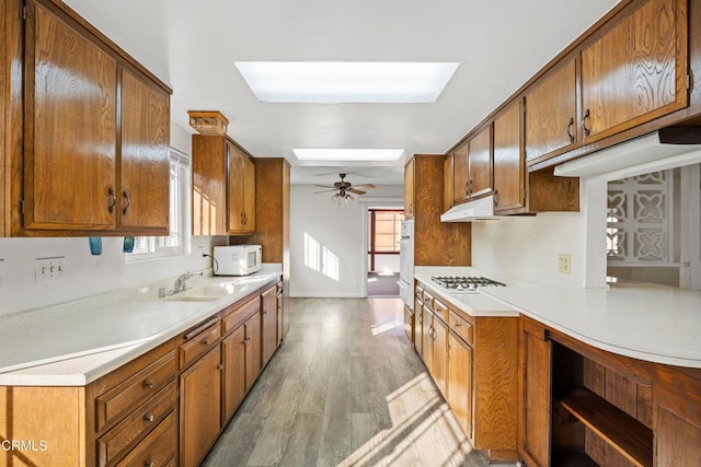 kitchen with a skylight, sink, light wood-type flooring, ceiling fan, and gas stovetop