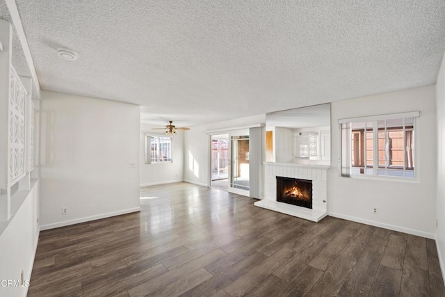 unfurnished living room featuring ceiling fan, a textured ceiling, dark hardwood / wood-style flooring, and a fireplace