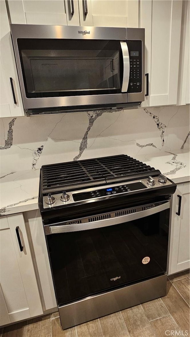 kitchen with tasteful backsplash, light stone countertops, appliances with stainless steel finishes, and white cabinets