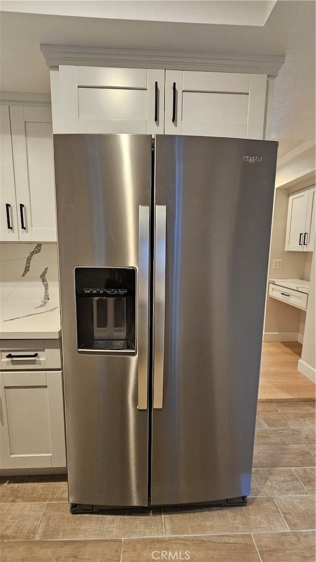 kitchen with white cabinetry, stainless steel fridge with ice dispenser, and light stone countertops