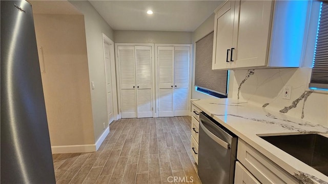 kitchen with sink, tasteful backsplash, white cabinets, stainless steel dishwasher, and light wood-type flooring