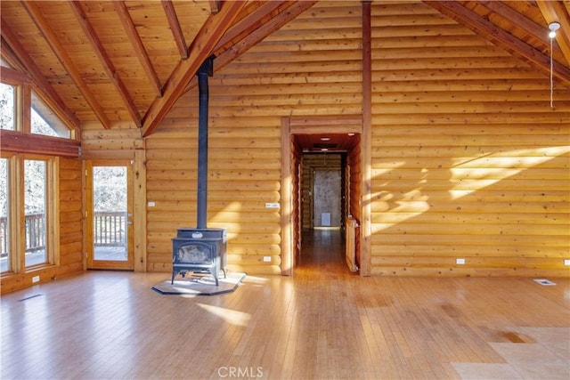 unfurnished living room with beam ceiling, high vaulted ceiling, a wood stove, and log walls