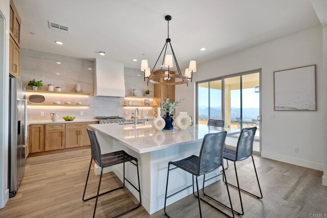 kitchen with backsplash, custom range hood, a breakfast bar area, and light wood-type flooring