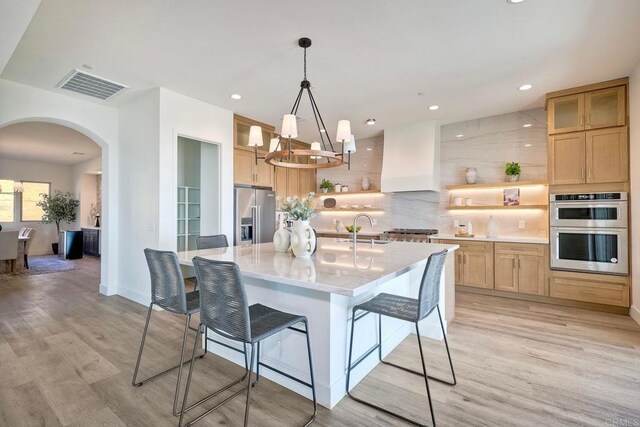 kitchen featuring premium range hood, a center island with sink, appliances with stainless steel finishes, hanging light fixtures, and sink