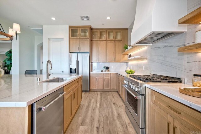 kitchen with stainless steel appliances, tasteful backsplash, light wood-type flooring, custom range hood, and sink