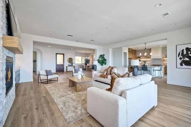 living room featuring an inviting chandelier, a stone fireplace, and light hardwood / wood-style flooring