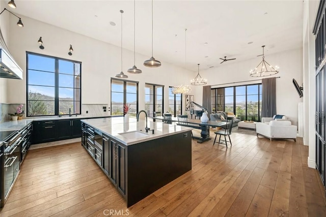 kitchen with light hardwood / wood-style floors, backsplash, a kitchen island with sink, hanging light fixtures, and sink