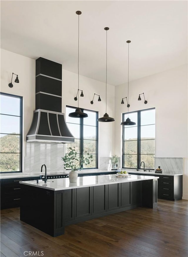 kitchen with decorative light fixtures, a kitchen island with sink, dark wood-type flooring, and decorative backsplash