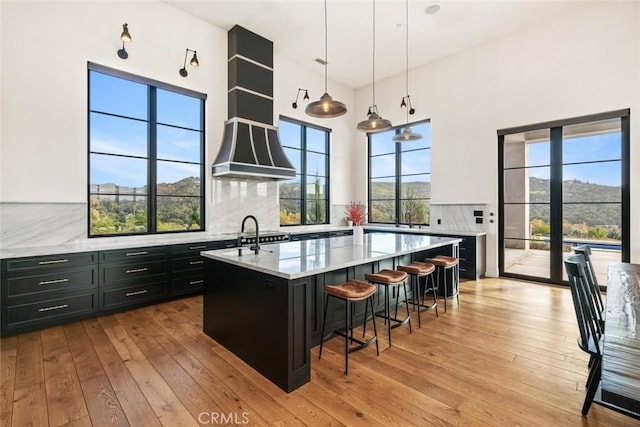 kitchen featuring a center island with sink, decorative backsplash, light stone countertops, and pendant lighting