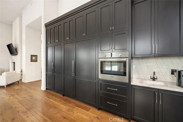 kitchen featuring tasteful backsplash, sink, stainless steel oven, light stone counters, and light hardwood / wood-style flooring