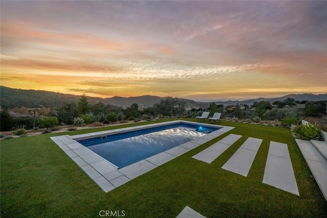 pool at dusk with a patio area, a mountain view, and a yard