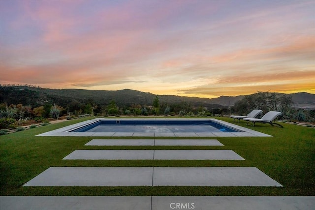 pool at dusk with a lawn, a patio area, and a mountain view