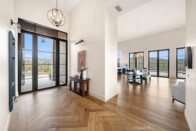 foyer entrance featuring a towering ceiling, parquet flooring, and a chandelier