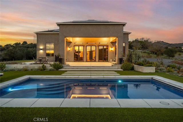 back house at dusk with a swimming pool with hot tub and a patio