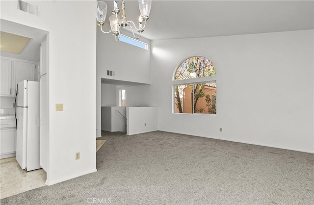 unfurnished living room featuring light carpet, a towering ceiling, and a chandelier