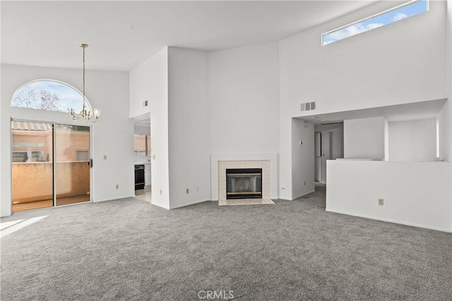 unfurnished living room with carpet, a tile fireplace, a high ceiling, and a chandelier