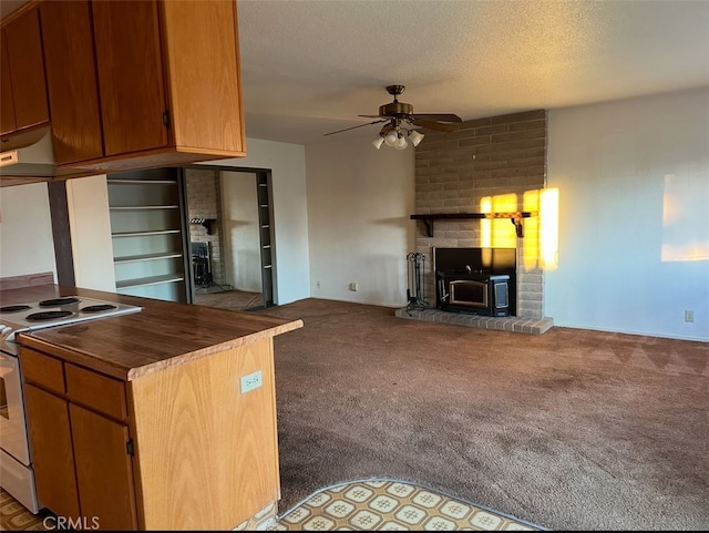 kitchen featuring a textured ceiling, dark colored carpet, a wood stove, ceiling fan, and stove