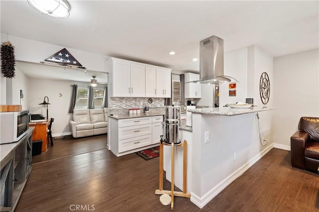 kitchen with kitchen peninsula, island exhaust hood, white cabinetry, a kitchen breakfast bar, and light stone counters