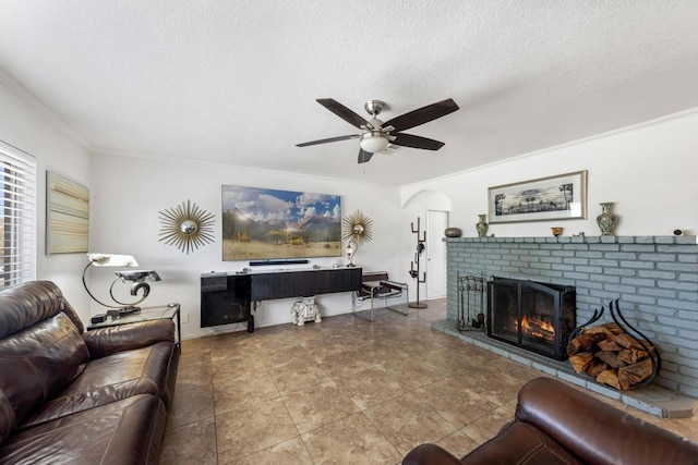 living room with ceiling fan, a brick fireplace, ornamental molding, and a textured ceiling