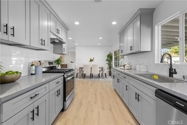 kitchen featuring stainless steel appliances, sink, gray cabinets, light wood-type flooring, and light stone counters