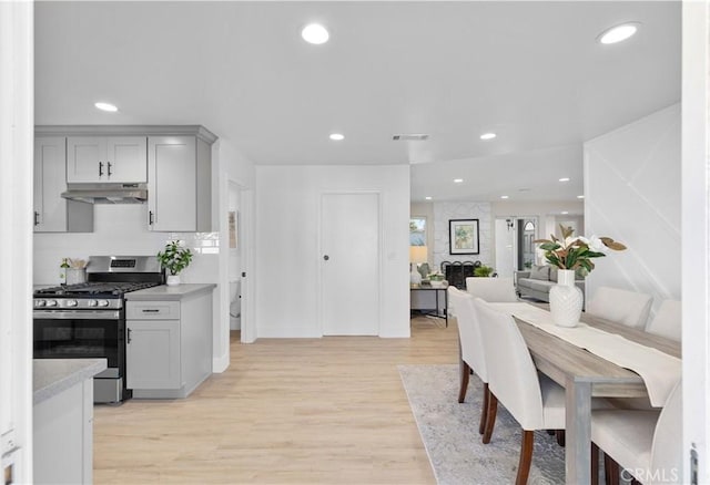 kitchen featuring light wood-type flooring, light stone counters, stainless steel range with gas stovetop, and gray cabinets