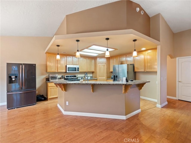 kitchen with light brown cabinetry, decorative light fixtures, and stainless steel appliances