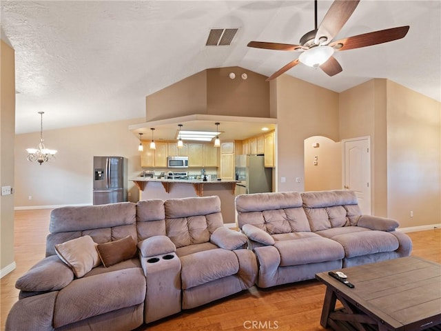 living room with vaulted ceiling, ceiling fan with notable chandelier, and light hardwood / wood-style floors