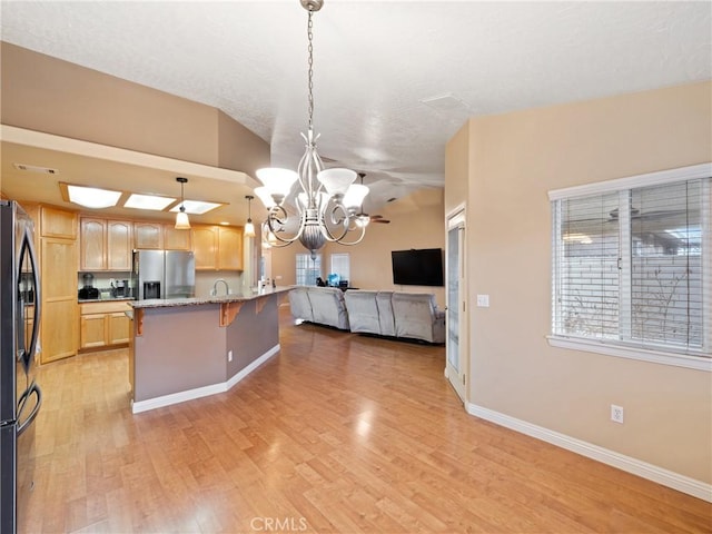 kitchen featuring stainless steel refrigerator with ice dispenser, light brown cabinets, hanging light fixtures, stainless steel fridge, and light stone counters