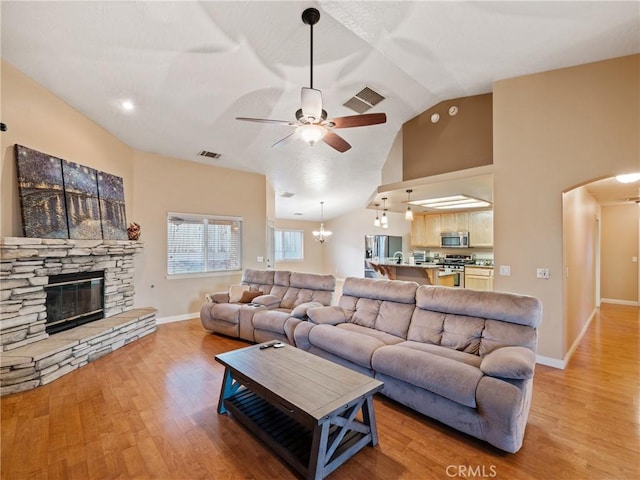 living room with ceiling fan, lofted ceiling, a stone fireplace, and light wood-type flooring