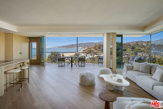 living room featuring wood-type flooring, a water and mountain view, a wealth of natural light, and wooden walls